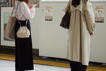 駅のホームで電車待ちの若い女性たちの姿