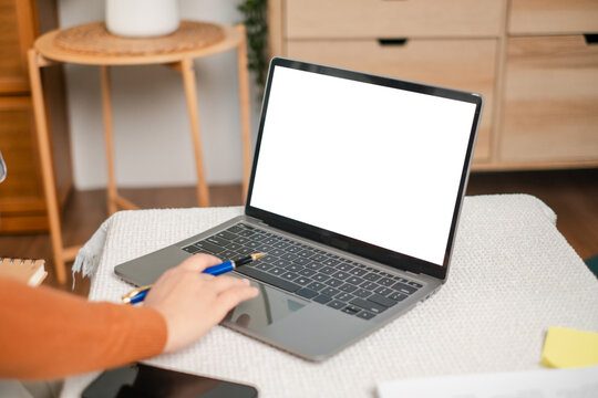 A person interacts with a laptop featuring a blank screen, set on a cozy table, ideal for remote work or online learning in a home environment.