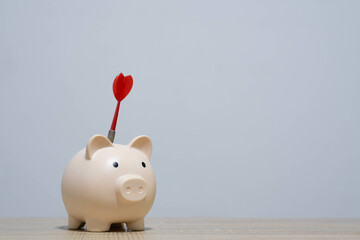 A creative concept image featuring a piggy bank with a dart stuck in it, representing financial goals, saving strategies, and investment ideas.