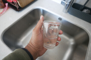 dirty Glass of water held above kitchen sink 