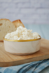 Fresh cottage cheese in bowl with bread on wooden board