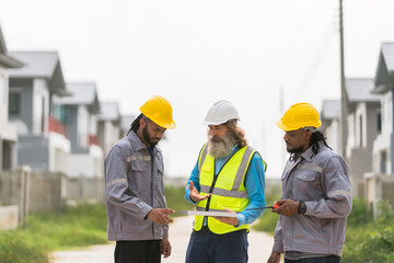 Three men in construction gear are standing on a road, looking at a piece of paper. They are wearing hard hats and safety vests