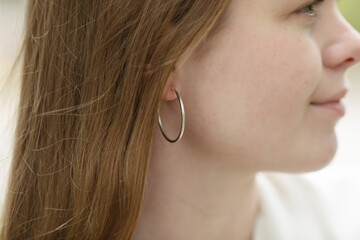 woman wearing a pair of silver hoop earrings. The earrings are large and are hanging from her...