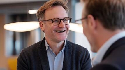Smiling men in business casual attire with glasses engaged in a friendly conversation in a modern office