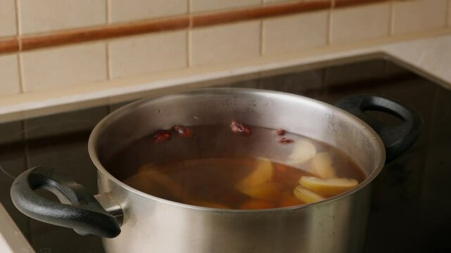 A person opens the lid of a saucepan, scoops up the compote with a ladle and pours it into the cup. Cooking delicious homemade compote on modern electric stove.