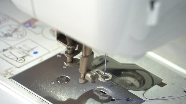 Inserting blue thread into the needle of a sewing machine. Hands that slowly move the fabric into the process of embroidering the name. White clothes with a plaid border.