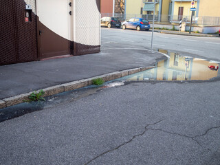 Urban reflection: residential block and parked cars mirrored in rainwater puddle on Cremona street