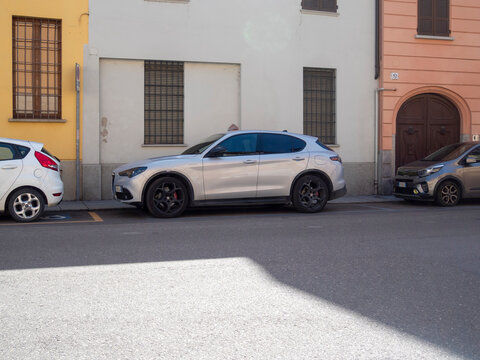 Silver Alfa Romeo Stelvio Quadrifoglio 2.9L V6 Bi-Turbo Parked on Street Surrounded by Buildings with Various Colors and Architecture Showcasing City Urban Landscape with Interesting Window Designs