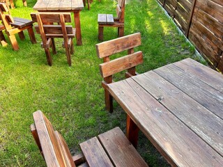 Fototapeta premium Wooden tables and chairs arranged on a green lawn in a quiet outdoor seating area surrounded by a wooden fence