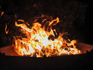Night photo of a bonfire in an iron fire bowl. Photography of flame of burning wood on black background.