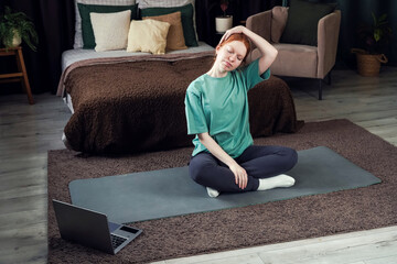A woman is performing a mountain climber exercise on a mat at home, following an online workout on her laptop. 