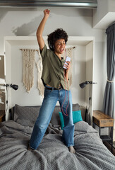 Young happy funky African American woman, funny gen z Afro girl in headphones singing in smartphone...