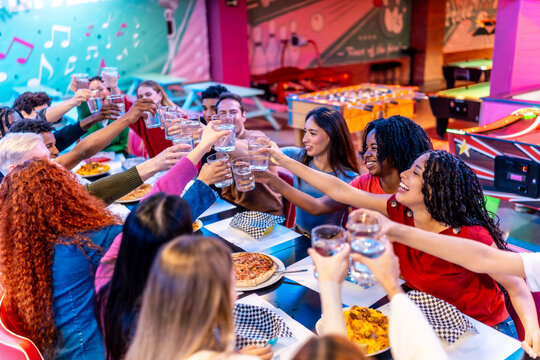 Happy multiethnic friends toasting drinks at bowling alley restaurant