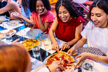 Happy multi ethnic friends sharing pizza and nachos at bowling alley