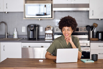 Young happy smiling African American woman student user customer using laptop computer elearning or hybrid working at home looking away, studying online sitting at kitchen table. Copy space.