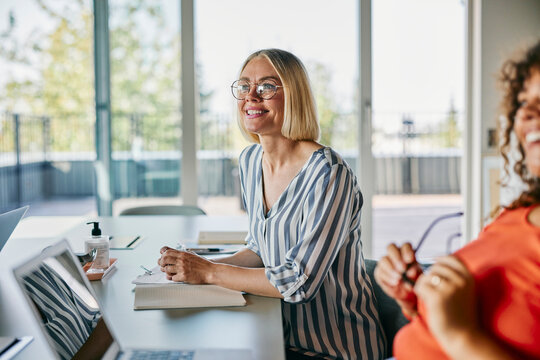 Creative input in progress. A blonde smiling woman offers ideas in a vibrant workspace. The team supports each other with enthusiasm and focus.