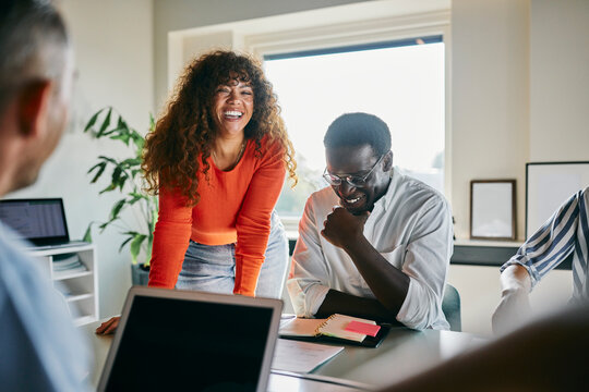 Creative input in progress. A smiling woman offers ideas in a vibrant workspace. The team supports each other with enthusiasm, smiles and focus.