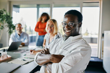 Happy business team collaborating in a modern bright office environment. A smiling black man sits confidently adding warmth and energy to the group. 