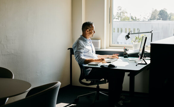 Modern Office Workspace, With Professional moden man in a blue shirt, Working at Desk by the Window. 