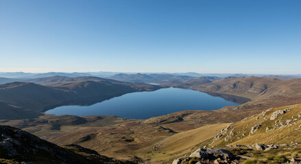 Fototapeta premium Serene Mountain Lake Surrounded by Majestic Hills and Clear Sky