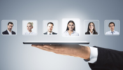 Businessman's hand holding tablet with virtual profiles of diverse professionals on light background, symbolizing digital recruitment concept.