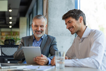 Mature businessman using a digital tablet to discuss information with a younger colleague in a...