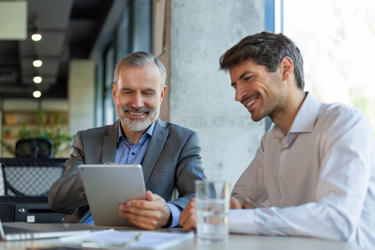 Mature businessman using a digital tablet to discuss information with a younger colleague in a modern business office