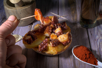 Hand picking a piece of Galician-style octopus tapa with a toothpick. Traditional Spanish seafood dish with paprika and potatoes, close-up