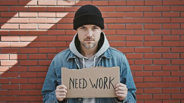 A sad, jobless person wearing a black cap hoodie holding a card text with NEED WORK 