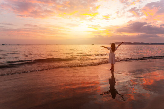 Young Asian woman traveler relaxing and watching beautiful Sunset on the tranquil beach, Travel on summer vacation concept