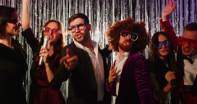 slow motion video of a group of happy smiling young people singing song into microphones having fun at disco party together at karaoke club. Funny friends dancing in modern nightclub. 4k video.