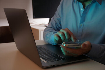 Businessman Using Smartphone and Laptop in Low Light Office