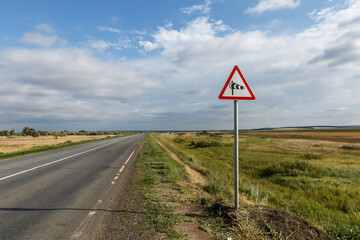Crosswind warning sign near an open road in a rural landscape with cloudy sky