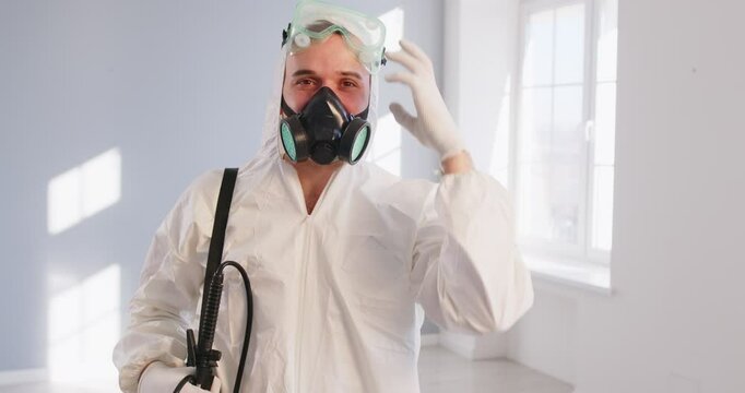 Pest control worker taking off protective glasses and mask, keeping thumb up and showing good results after disinfecting and fighting insects in house, spraying pesticides. Service man 