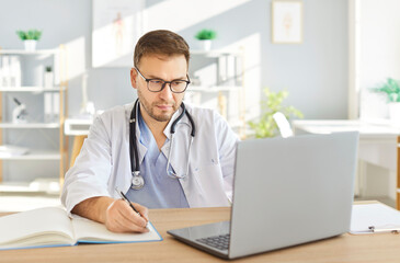 Focused male doctor or nurse working with a laptop and documents in a clinic office. Conducting research, reviewing prescriptions, and handling healthcare tasks with precision and dedication.
