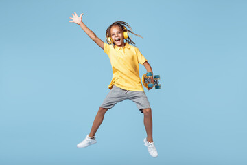 Fototapeta premium Gleeful little boy with african dreads listening music in headphones dancing over blue background.
