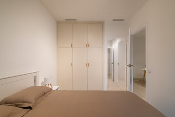 Minimalist bedroom with taupe bedding, white built-in wardrobe and two open doorways