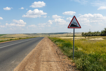 Road sign indicating steep gradient on rural highway with scenic landscape in the background