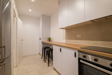 Modern kitchen perspective with bar counter, stools, white cabinetry and wood countertop finish