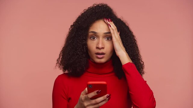 Shocked woman reading bad news on phone on pink background