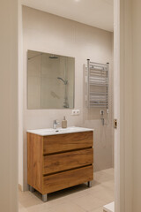 Bathroom view from hallway showing wood vanity, glass shower and chrome towel warmer
