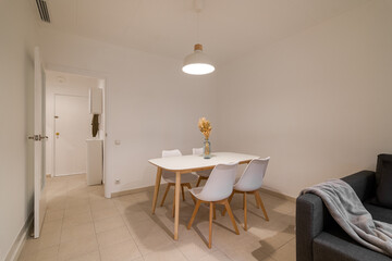 Compact dining zone with a white table and four matching chairs set beside a dark sofa in the living space
