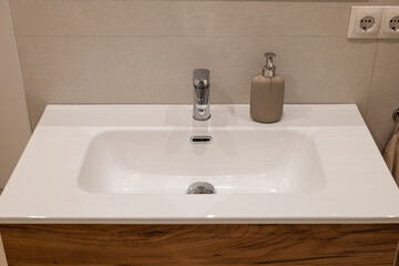 Top view of bathroom sink with chrome faucet, beige soap dispenser and wooden vanity base