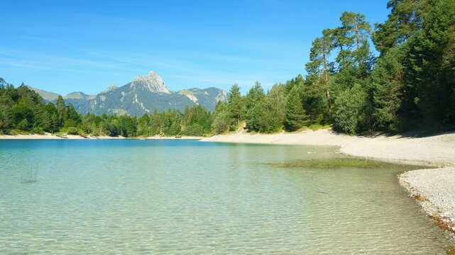 Calm lake Urisee in Tirol with vivid blue water, forest shoreline, and scenic mountain views, perfect summer relaxation setting
