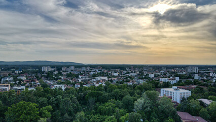Drone view of a charming city during spring sunset. Green trees, residential houses, and buildings glow in soft light, creating a peaceful and colorful urban scene.