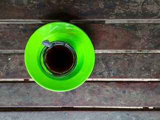 close up of a cup of black coffee and a green plate, on a wooden table