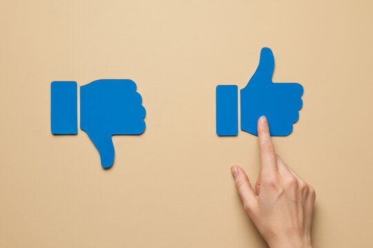 Like unlike concept hand finger pointing at thumbs up and thumbs down blue icons on beige surface - Powered by Adobe