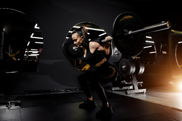 Powerful woman doing squats exercises with heavy barbell in the gym