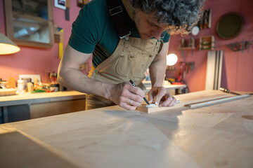 Meticulous carpenter drawing guidelines and drill points on wood surface for furniture construction in workshop. Accurate measurements, screw positioning, project plans, handmade marking, manual labor