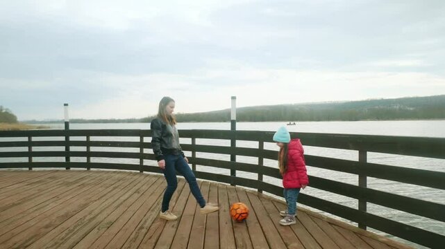 Mother and daughter at the pier near the water having fun. Mom with little girl playing a ball